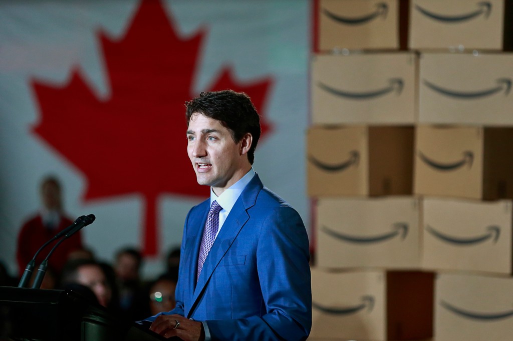 Justin Trudeau hablando en un podio rodeado de cajas de Amazon y una bandera canadiense al fondo