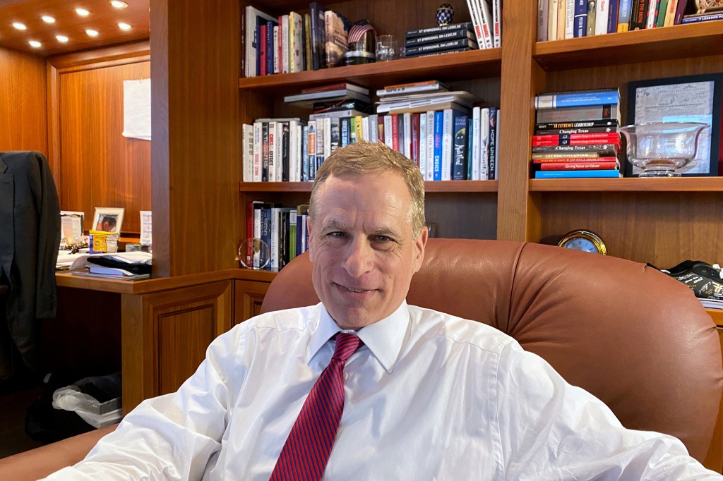Robert Kaplan sentado en una silla de oficina detrás de un escritorio con estantes de libros detrás de él