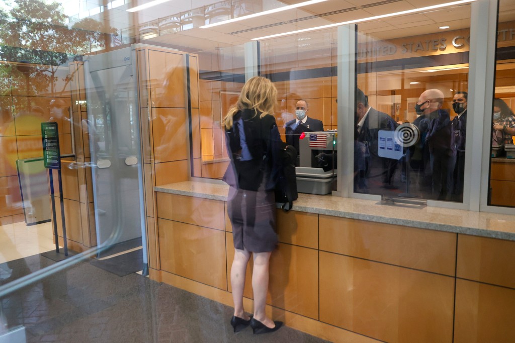 Elizabeth Holmes vista desde atrás mientras se para frente a las ventanas de vidrio en el mostrador de seguridad en un juzgado.