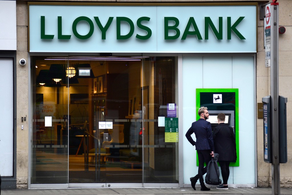 Exterior de un Lloyds Bank en Londres con dos personas de pie en un cajero automático 