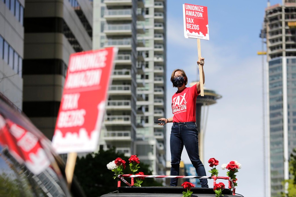 Un manifestante de Amazon de pie encima de un automóvil con un cartel.