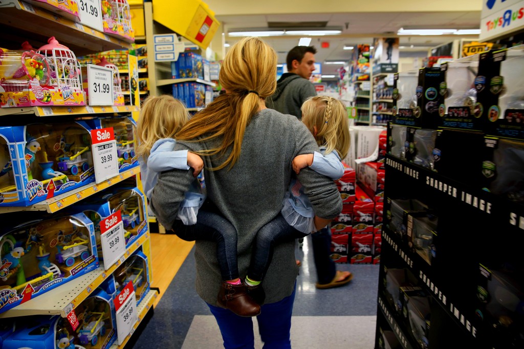 Una mujer que sostiene a dos niños pequeños en sus brazos mientras compra en una tienda de juguetes.