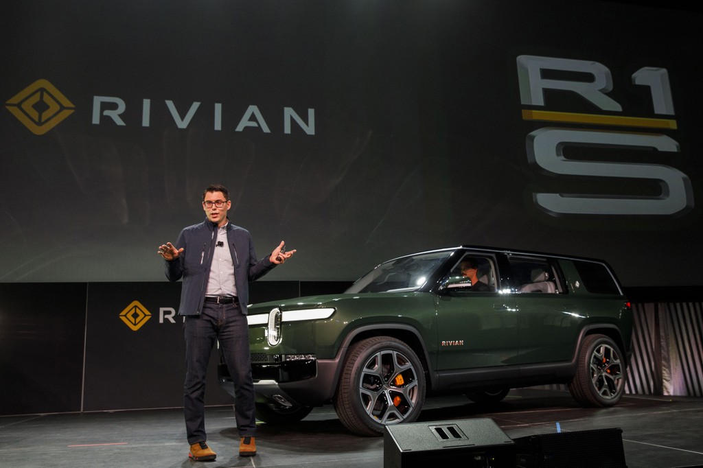 Un hombre está en el escenario junto a una camioneta eléctrica con el nombre y el logotipo de Rivian en la pantalla al fondo