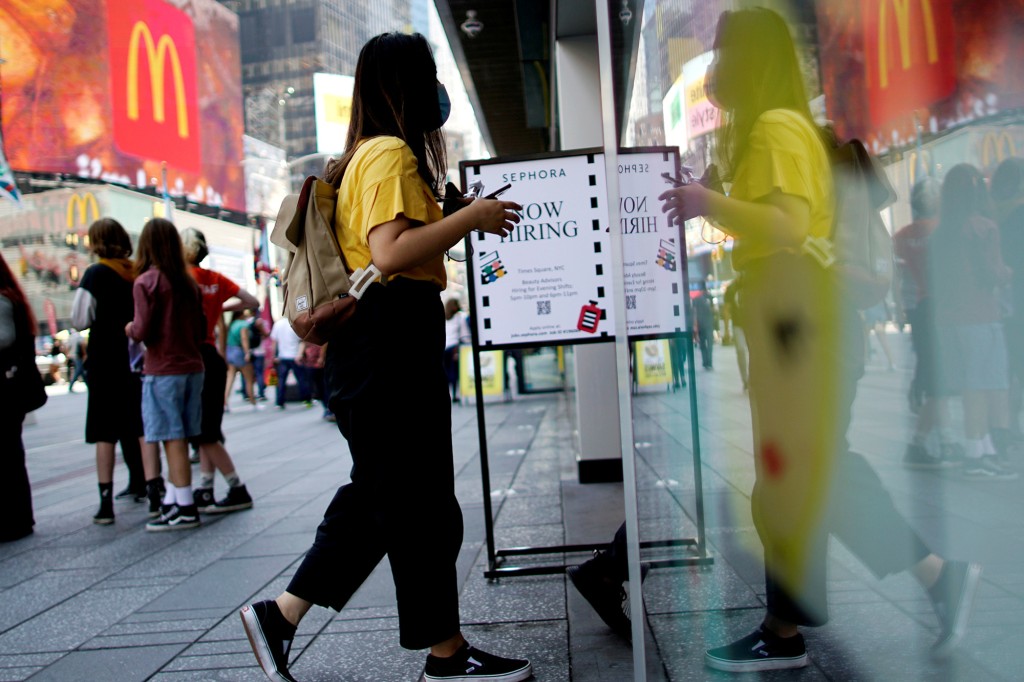 Una mujer entra en una tienda junto a un cartel que anuncia vacantes en Times Square