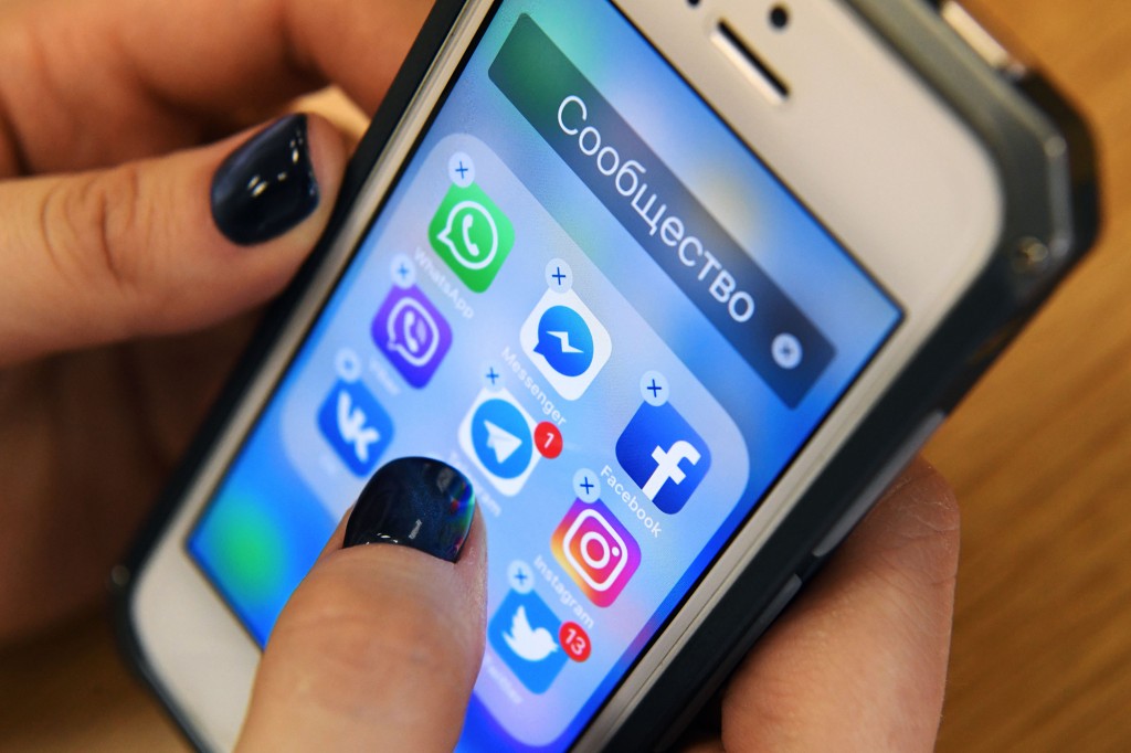 Una mujer sostiene un teléfono inteligente con letras rusas encima y los íconos de Facebook y aplicaciones de redes sociales