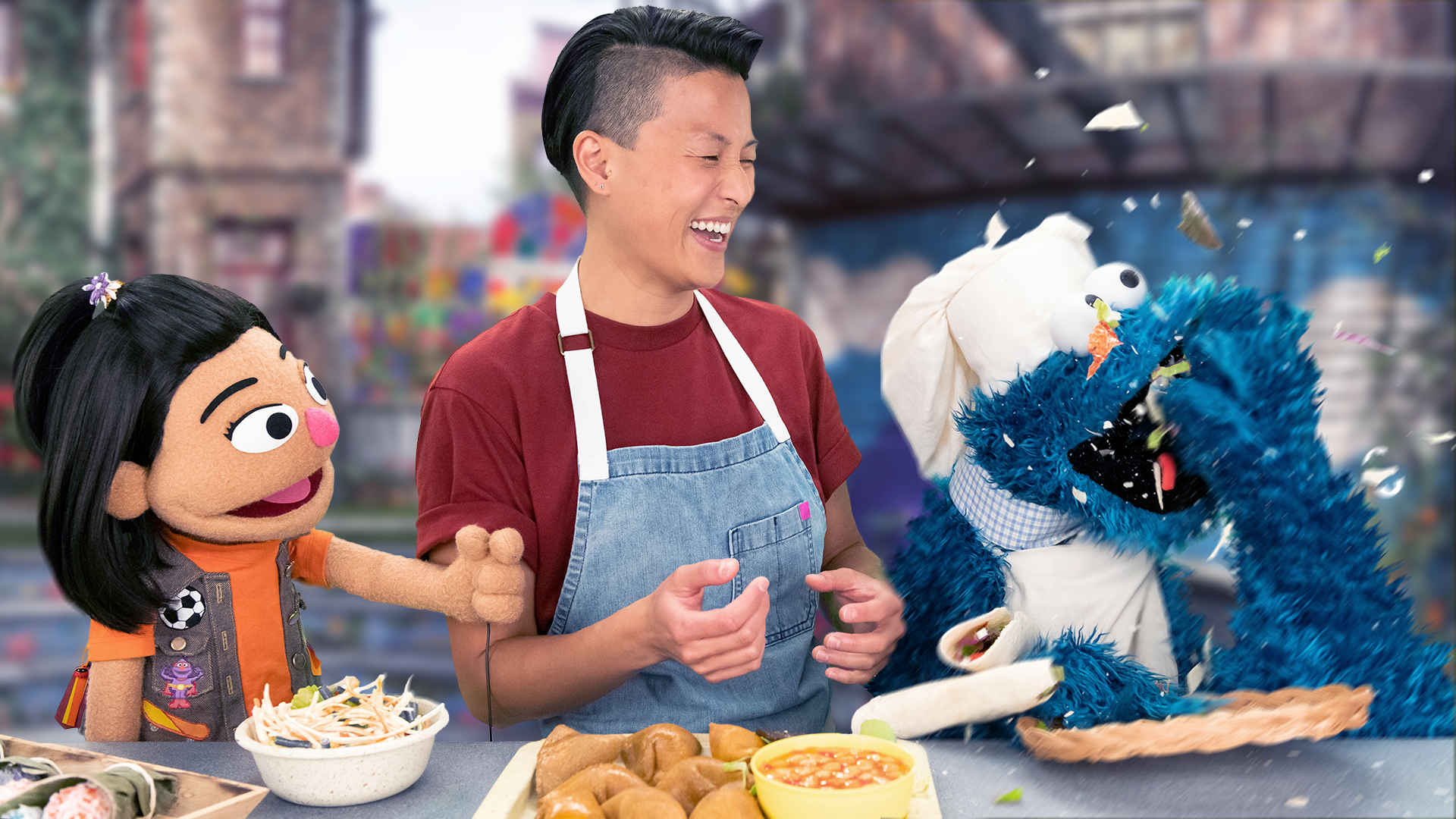 La chef Melissa King, el muppet Ji-Young y el Monstruo de las galletas se paran junto a una mesa de comida mientras el Monstruo de las galletas devora comida.