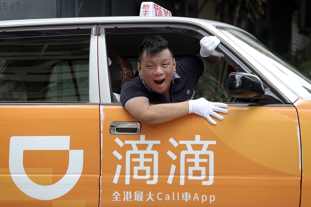 Un hombre sonriente se asoma por la ventana de un taxi Didi 