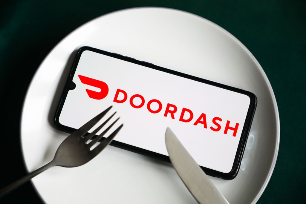 Un plato con un cuchillo y un tenedor apoyado en un teléfono inteligente que muestra la aplicación Doordash.