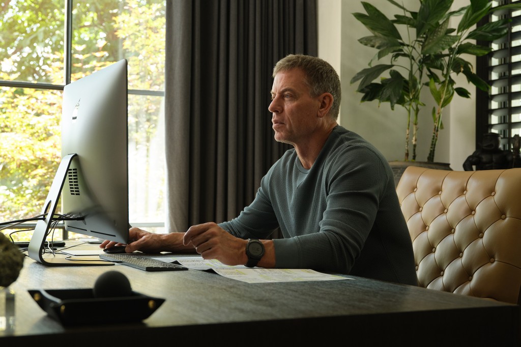 Aikman sentado en su escritorio, mirando la pantalla de una computadora.