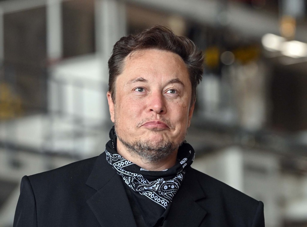 Elon Musk con una chaqueta oscura y un pañuelo blanco y negro alrededor del cuello