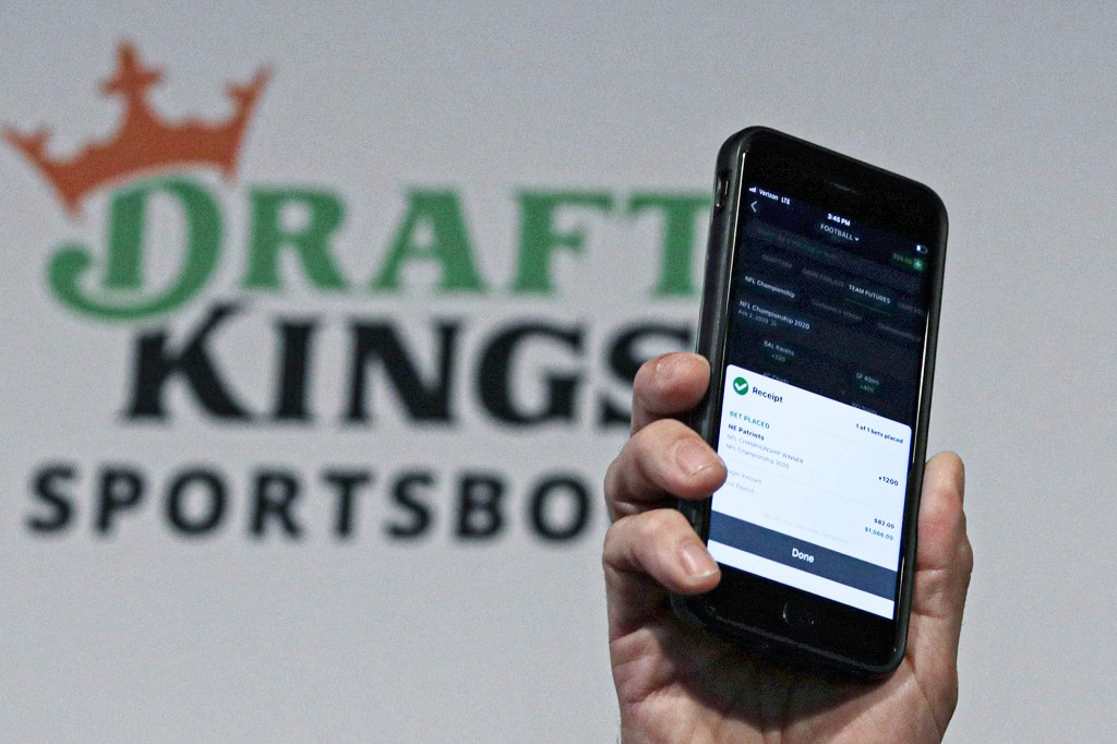 La aplicación DraftKings se muestra en un teléfono inteligente contra el logotipo en el fondo