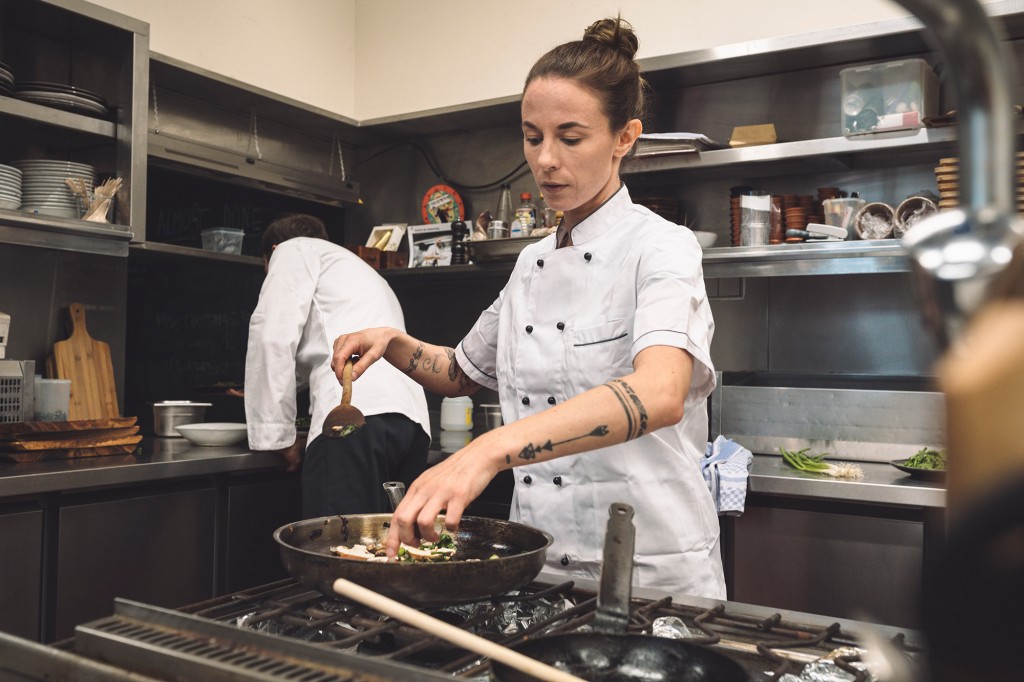 Un cocinero con uniforme blanco prepara una comida en una sartén