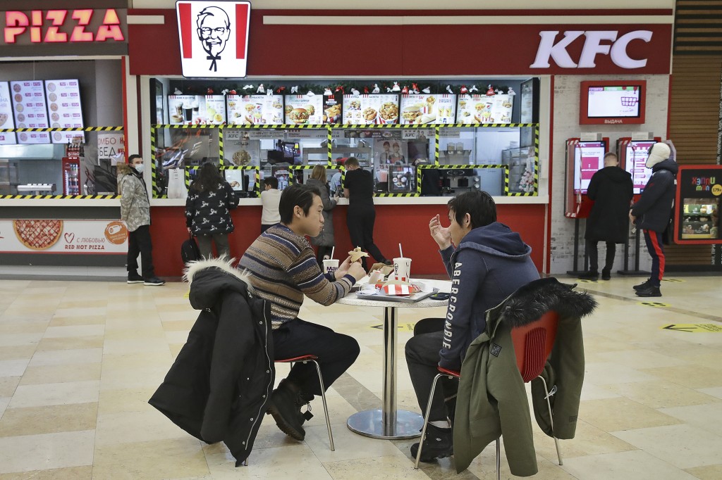 Dos hombres comiendo en un patio de comidas frente a un mostrador de KFC en Rusia.